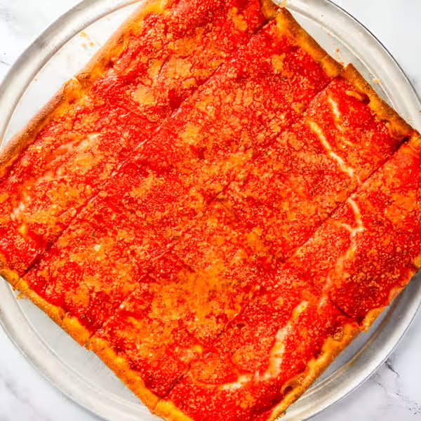 A square Dragos Pizza, cut into slices, with bright red sauce and a sprinkle of cheese.