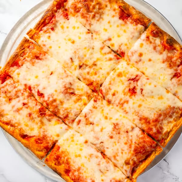 Square-cut Dragos Pizza with melted cheese and red sauce on a metal pan.