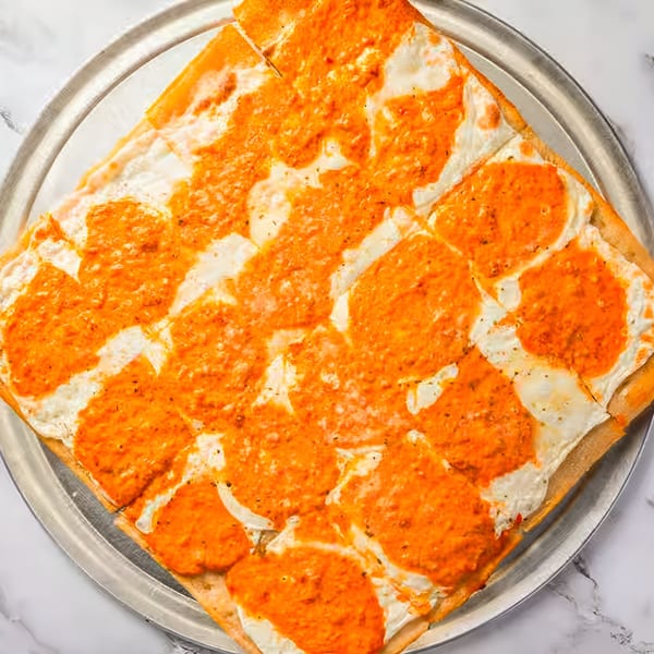 Square Dragos Pizza with white cheese and orange sauce, cut into individual slices on a metal tray.