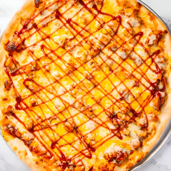 Close-up of a Dragos Pizza BBQ chicken pizza with melted cheese and a drizzle of sauce.