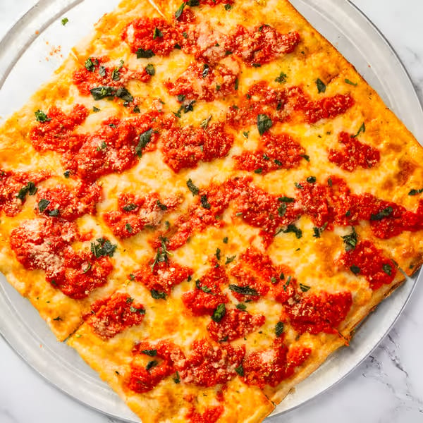 Square Dragos Pizza with bright red sauce, melted cheese, and fresh basil on a metal tray.