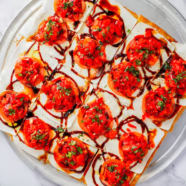 Square pizza slices topped with fresh mozzarella, sliced tomatoes, bruschetta, and balsamic glaze.